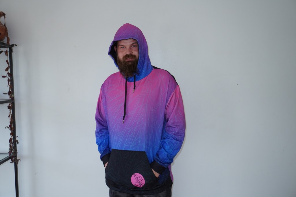  Model in a pink and blue gradient hoodie standing against a plain white wall.